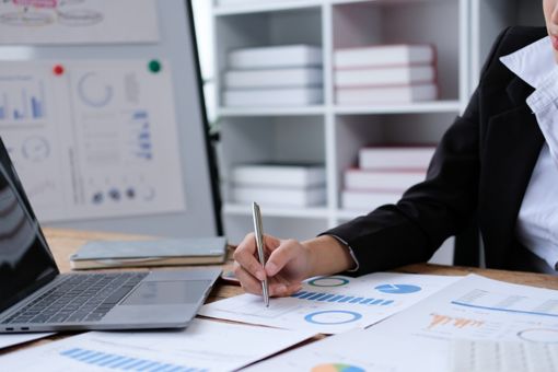 A woman is sitting at her desk with a computer and papers with graphs.